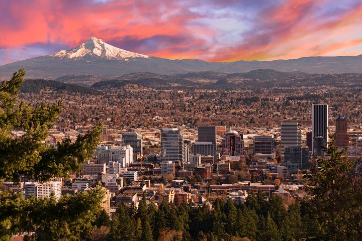 City skyline at sunset with a snow-capped mountain in the background and pink clouds overhead