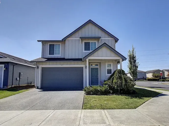 Suburban two-story house with blue garage door, front porch, and a small lawn on a sunny day