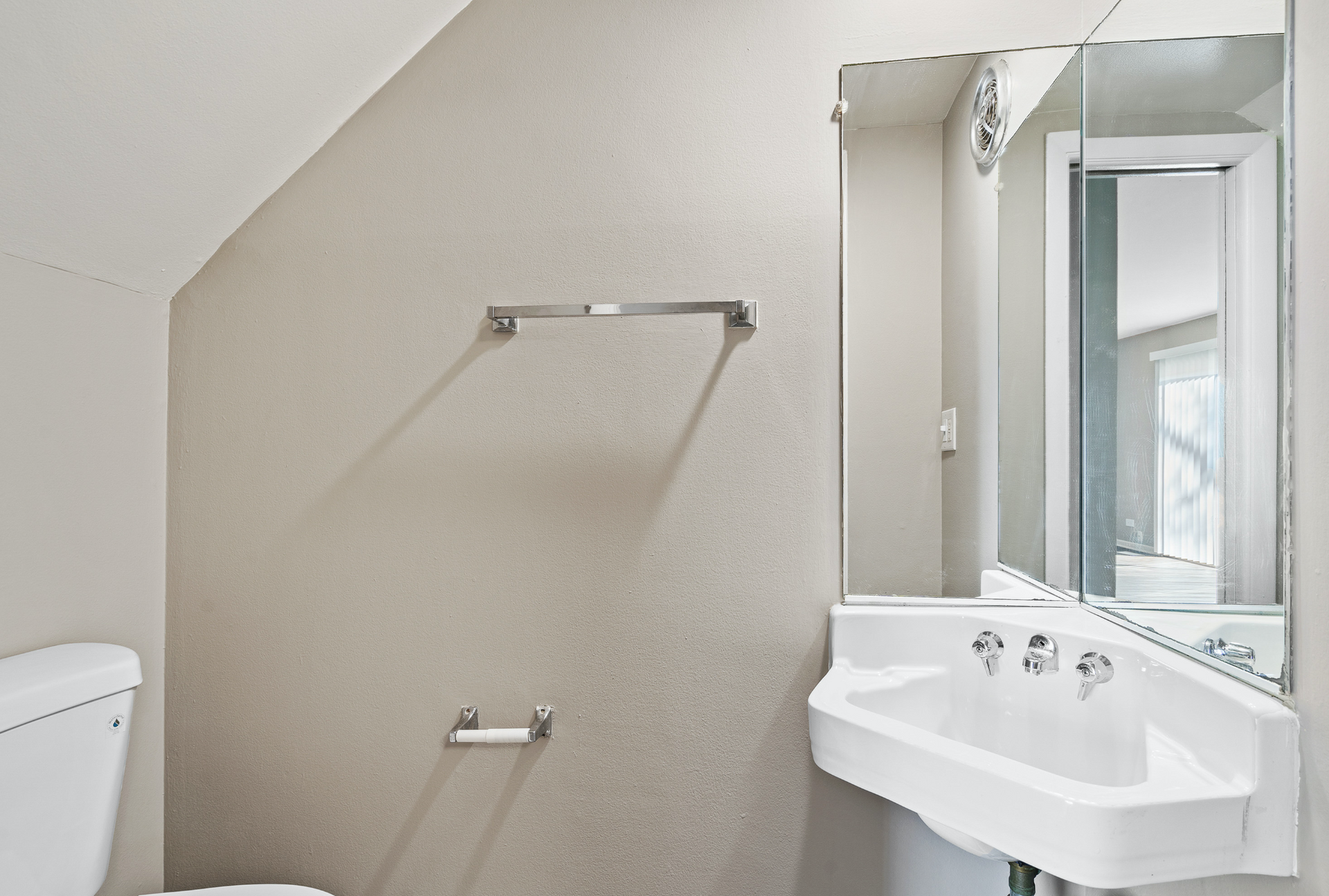 Small bathroom with a white sink, large mirror, toilet, and towel bar on beige walls.