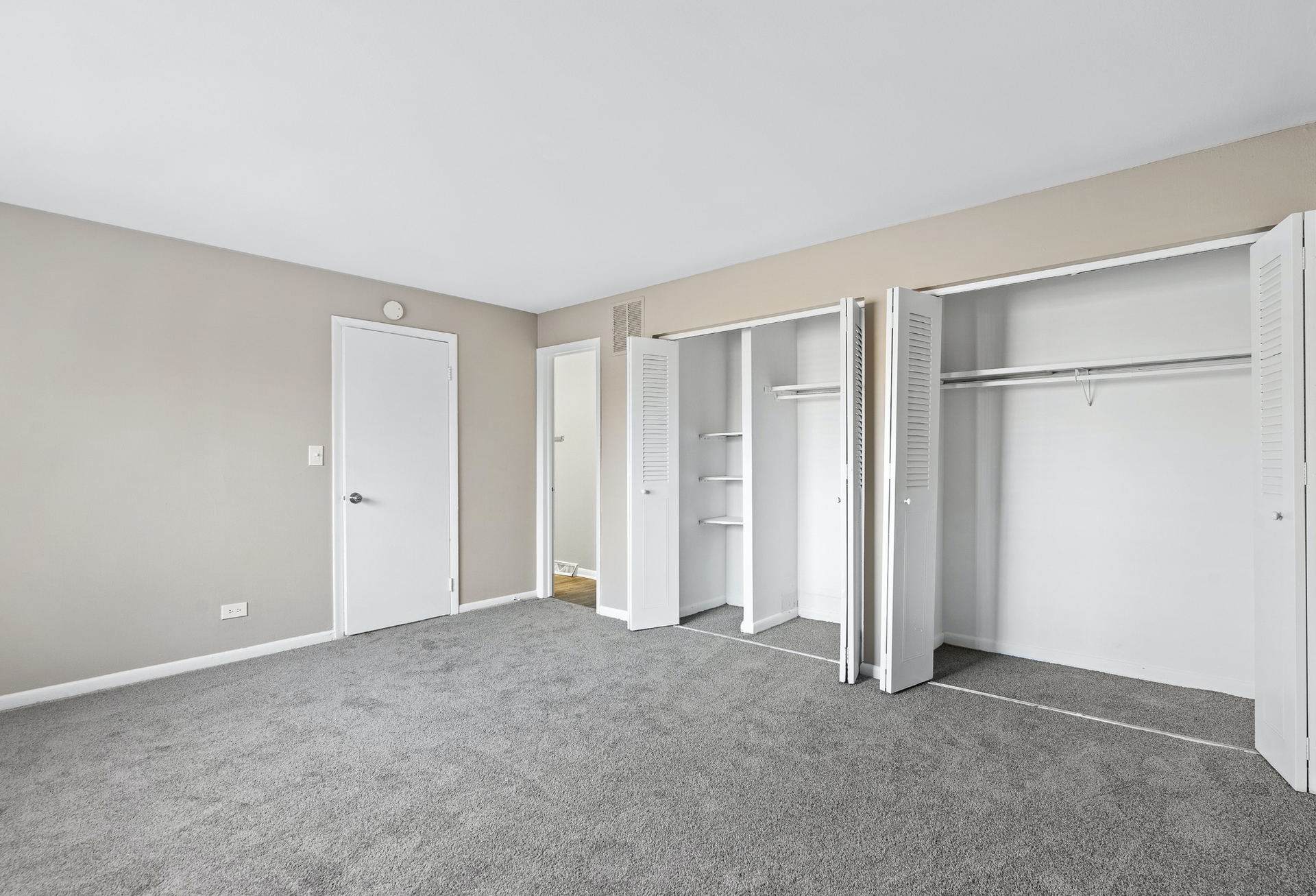 Vacant bedroom with beige walls, gray carpet, and open double closets.