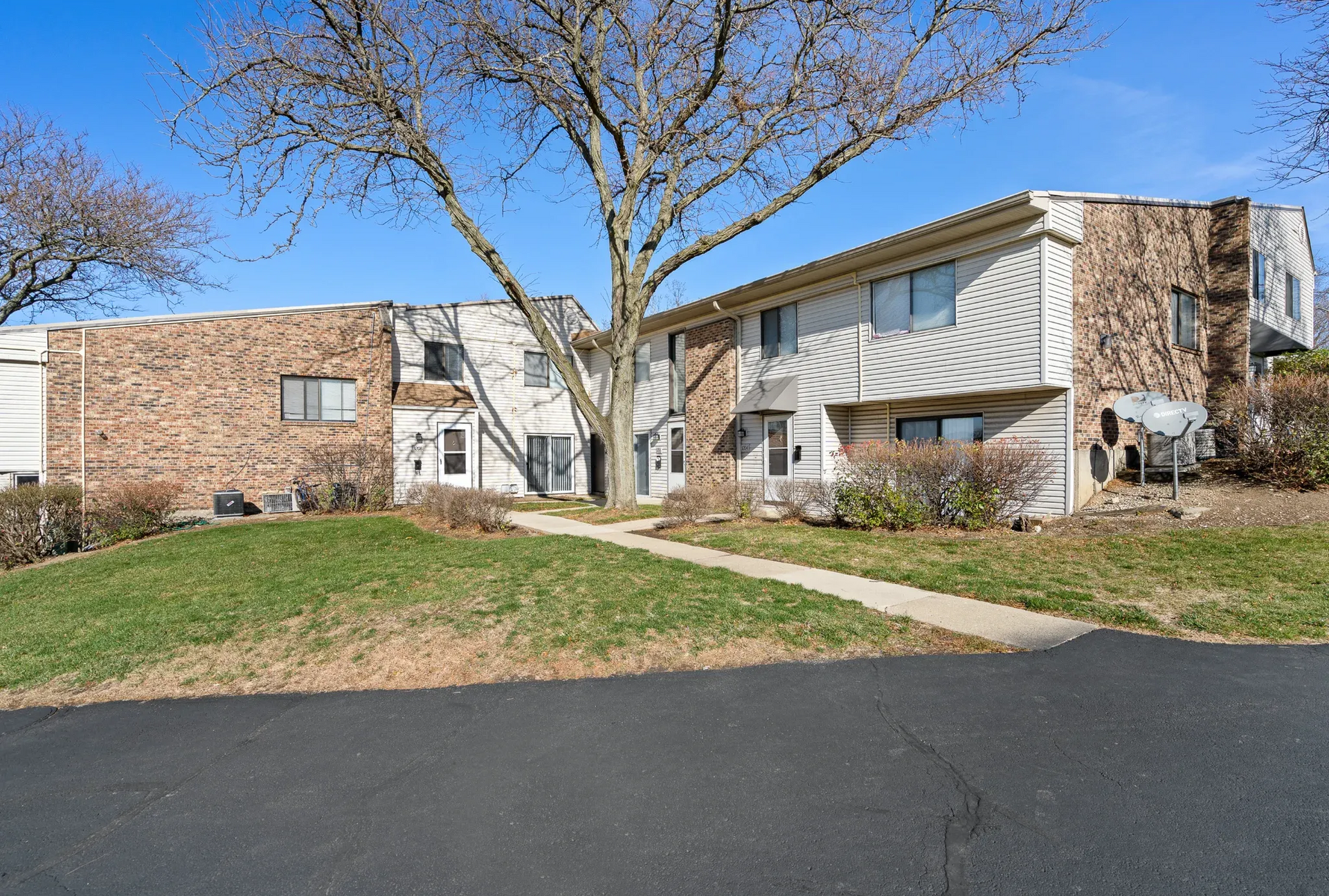Exterior view of a multi-unit apartment building with brick and beige siding, trees, and a walkway.