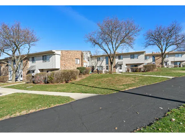 Row of two-story apartment buildings on a grassy hill with a paved road at Townhomes at Highcrest in Woodridge, IL.