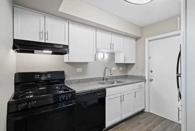 Small white kitchen with black appliances, gray countertops, and light wood floors at Townhomes at Highcrest.