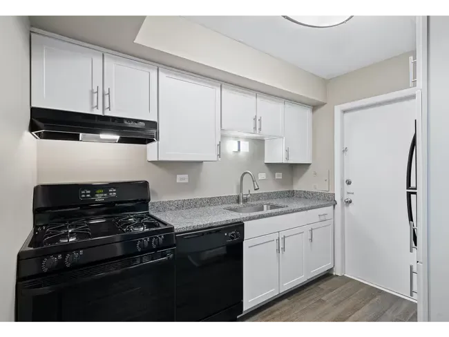 Small white kitchen with black appliances, gray countertops, and light wood floors at Townhomes at Highcrest.