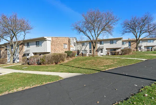 Row of two-story apartment buildings on a grassy hill with a paved road at Townhomes at Highcrest in Woodridge, IL.