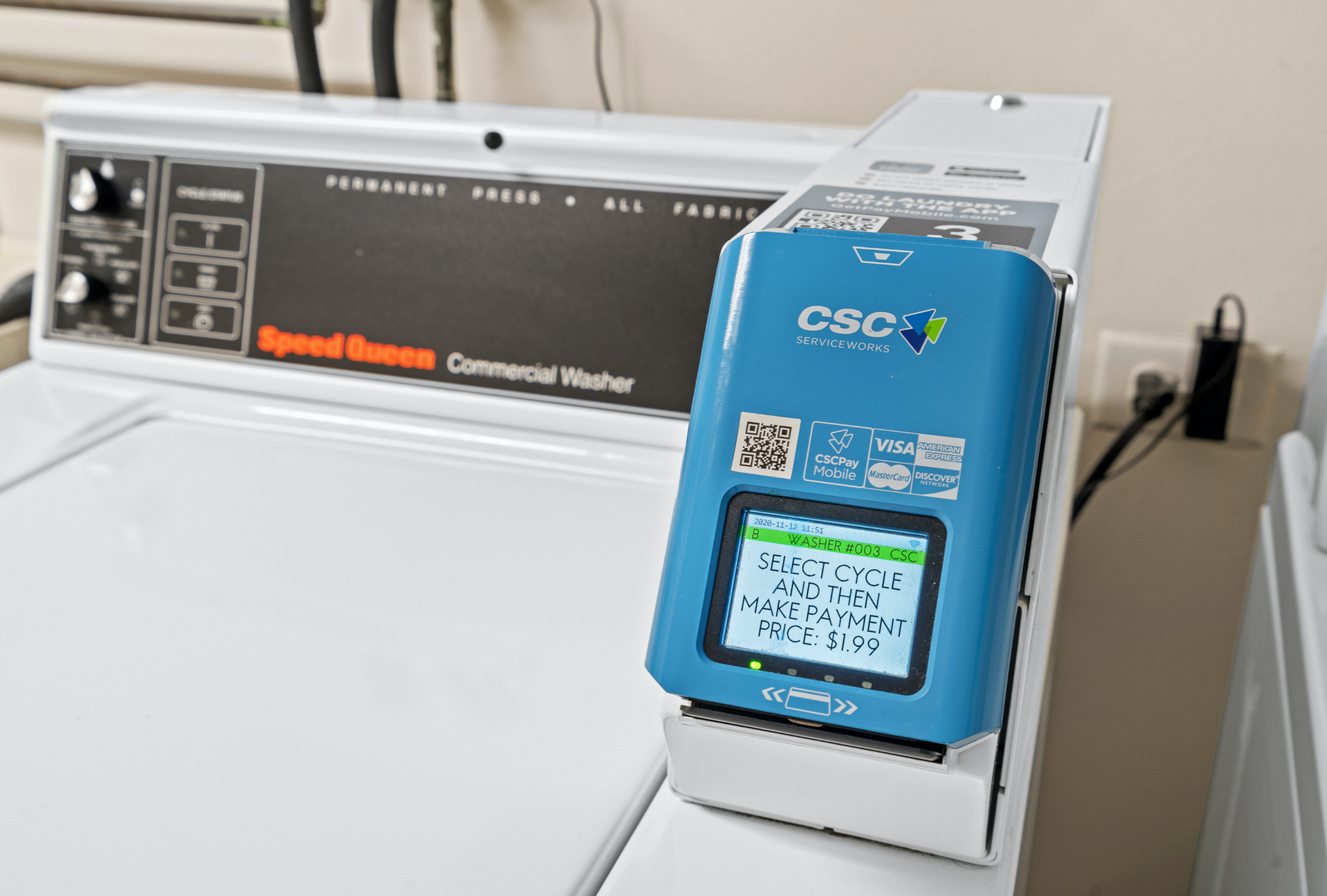Blue payment terminal on a Speed Queen commercial washer in a communal laundry room.