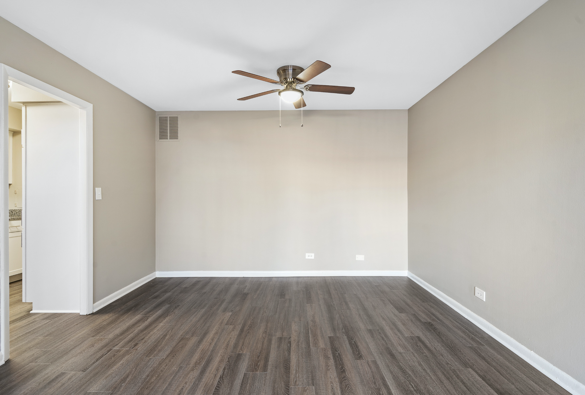 Living room with ceiling fan, beige walls, and dark wood-look flooring.