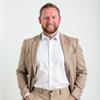 Jeremy Sheets, Colorado Springs real estate broker, standing in a tan suit with a white shirt against a plain light background
