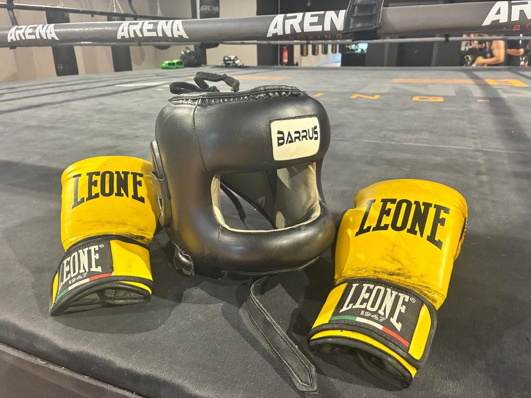 Attrezzatura da allenamento di boxe nera e gialla con guantoni e caschetto LEONE su un tappeto da ring.
