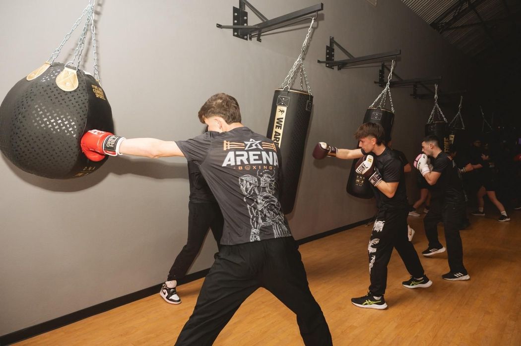 Persone che si allenano con i sacchi da boxe appesi in una palestra, con un istruttore in primo piano.
