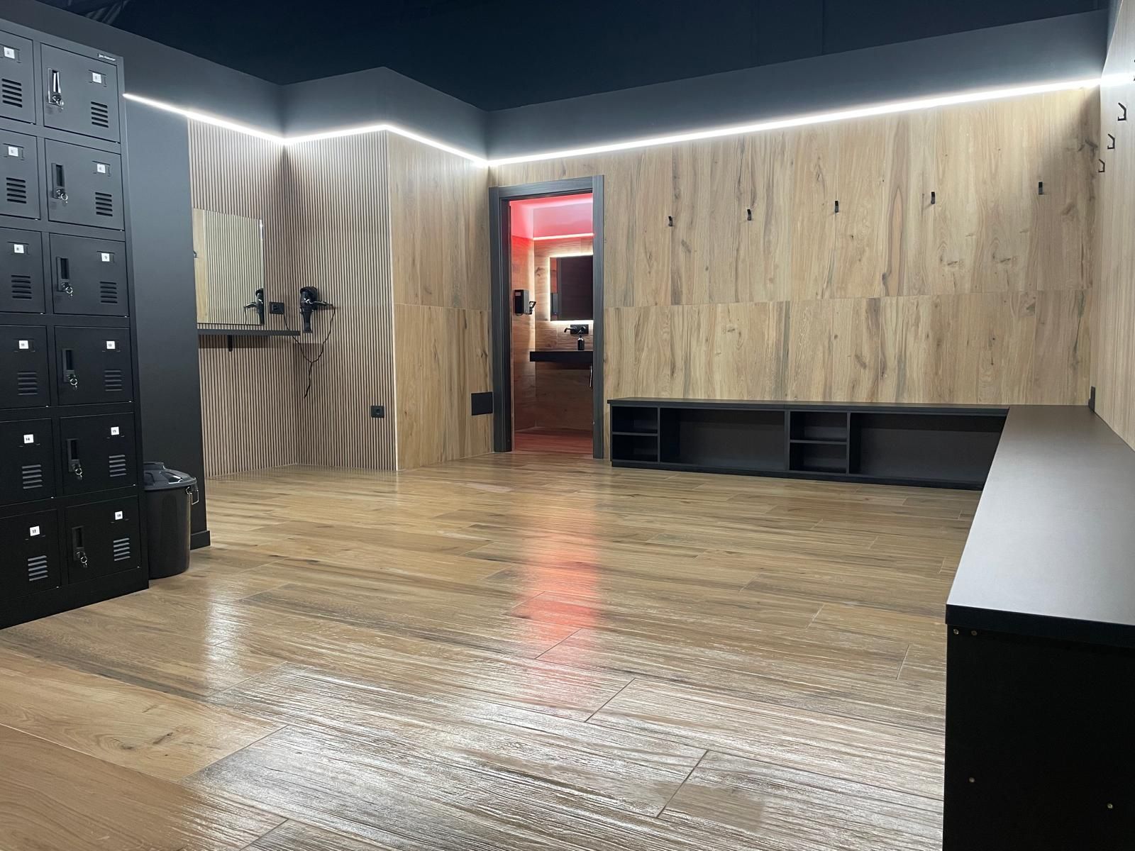 Camera moderna con pavimento in legno, armadietti neri e una parete rivestita in legno con una porta illuminata di rosso.