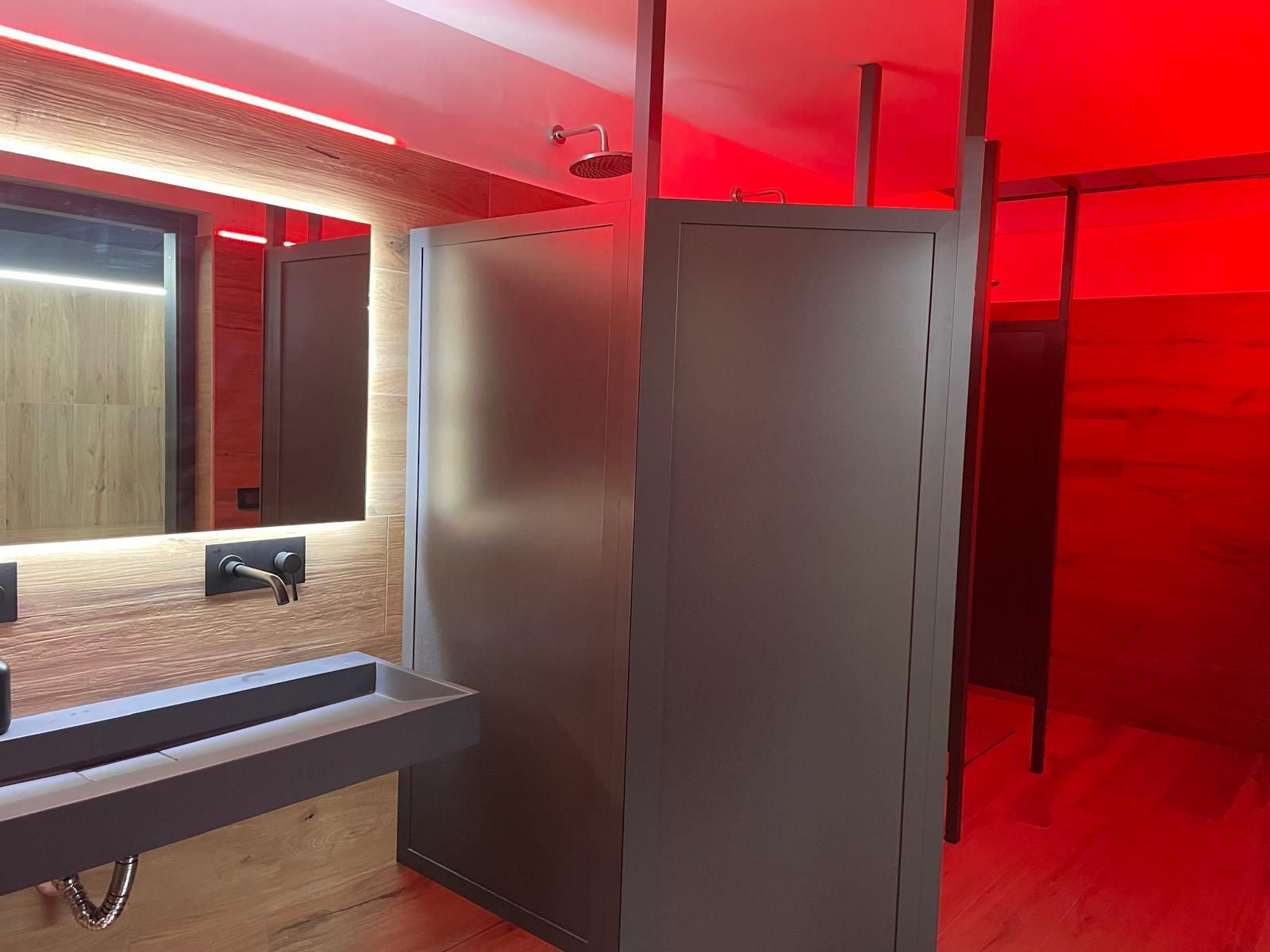 Bagno illuminato di rosso con lavandini, specchi e divisori tra le cabine.
