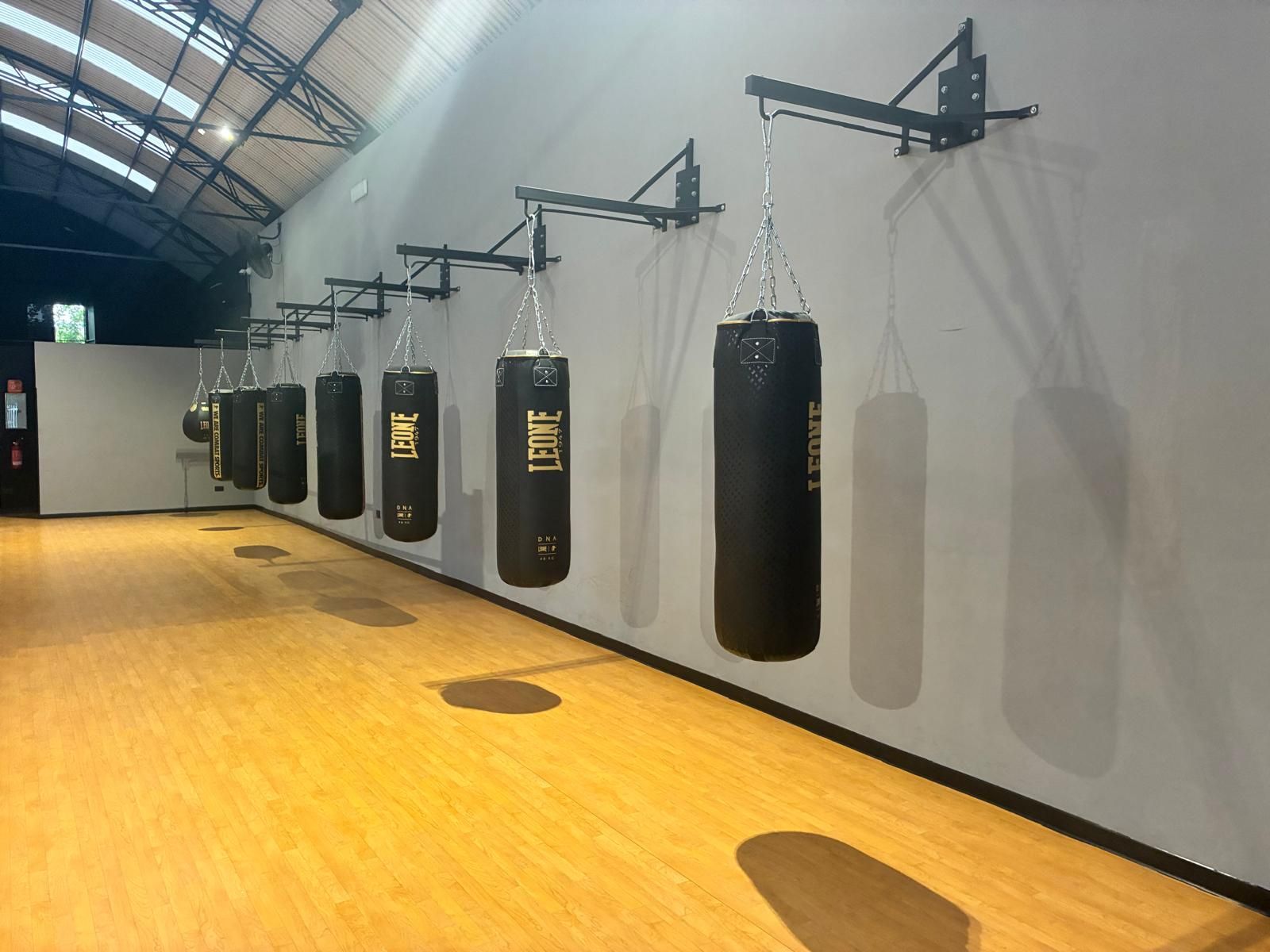 Palestra al coperto con sacchi da boxe appesi lungo una parete su un pavimento in legno.