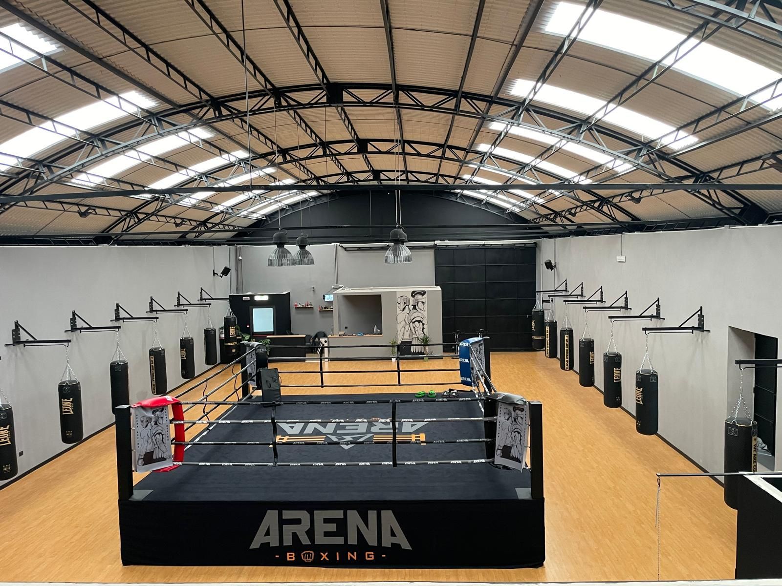 Palestra di boxe al coperto con ring centrale, pareti nere e soffitto alto a volta.