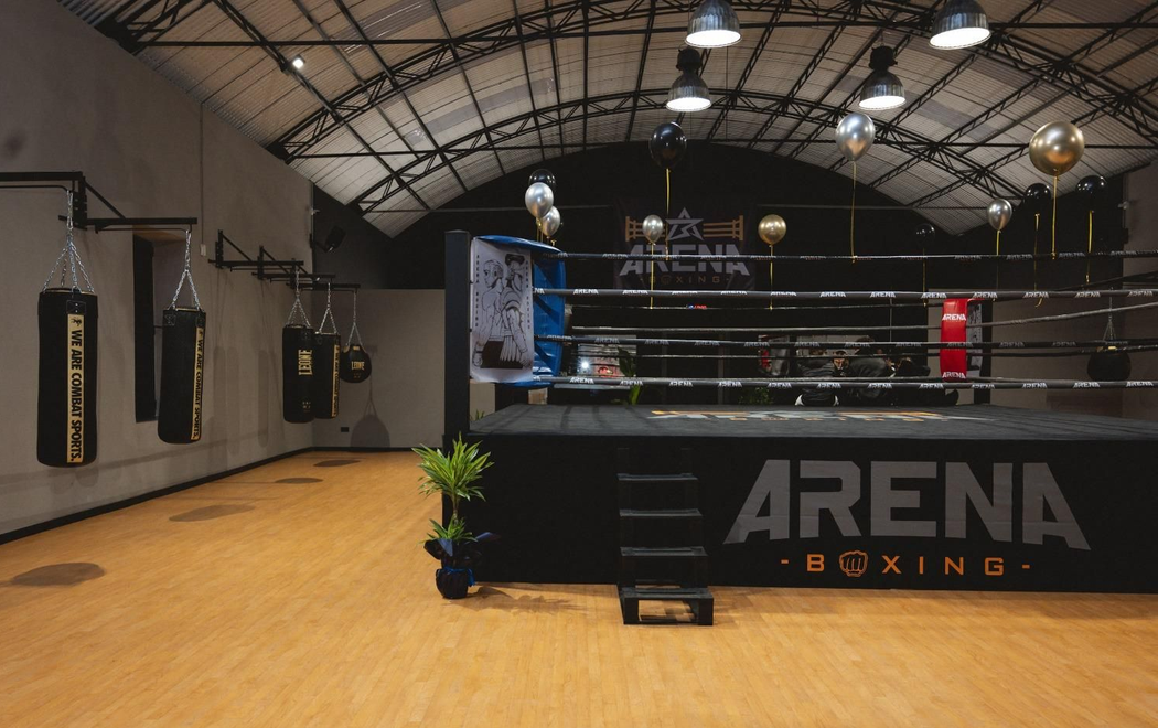 Palestra di pugilato vuota con ring, sacchi da boxe e una calda illuminazione dall'alto.