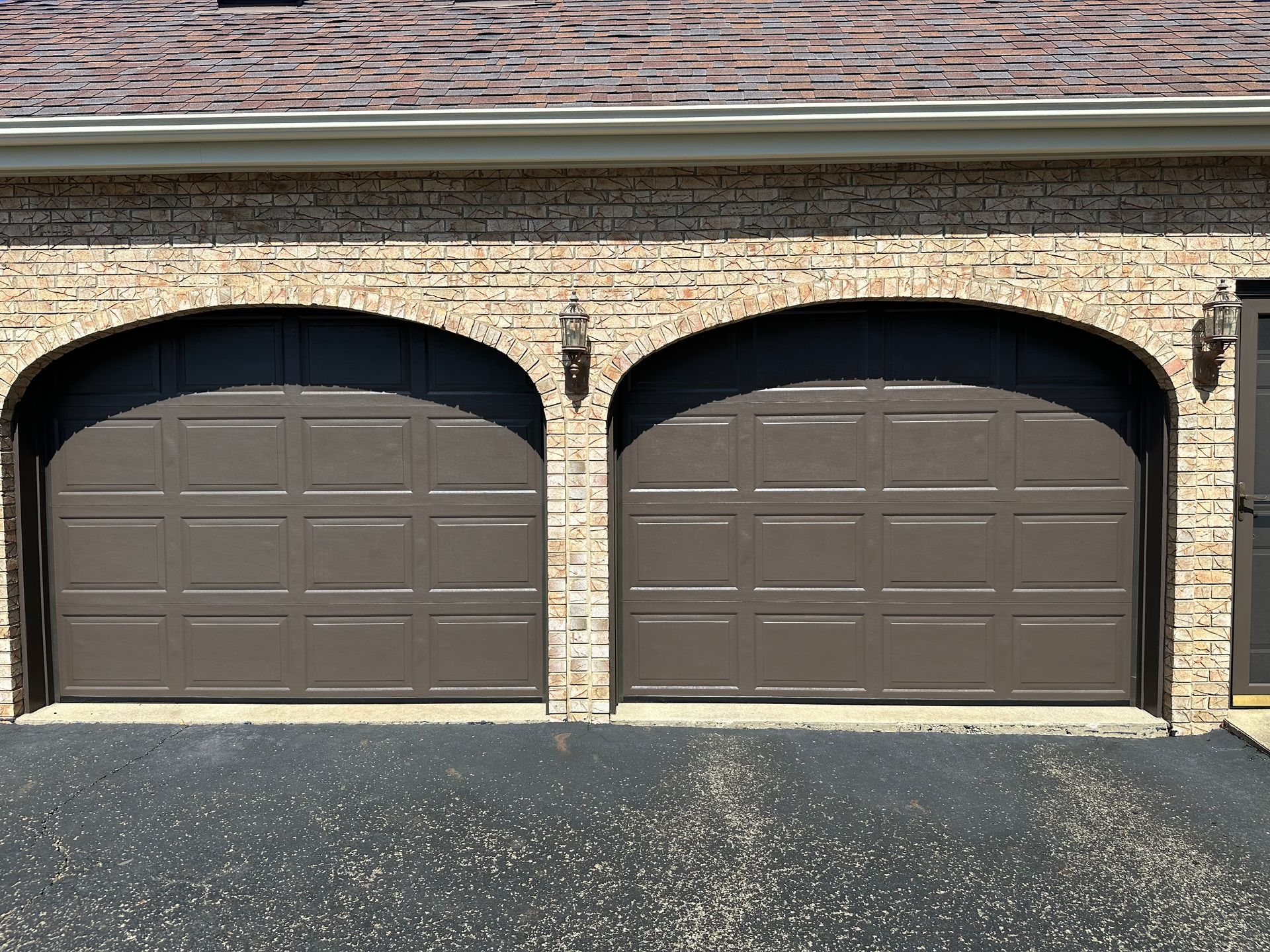 Two brown garage doors on a brick building