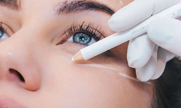 Gloved hand applying under-eye cosmetic treatment to a woman’s face with a white tool