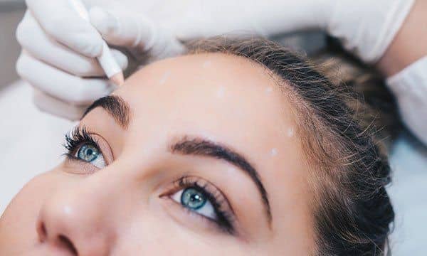 Gloved hands applying cosmetic treatment near a woman’s eyes and forehead
