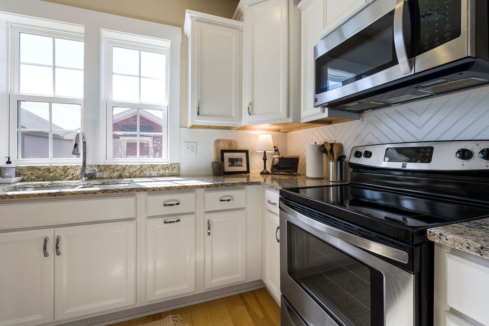 Modern white kitchen with stainless steel appliances, granite counters, and bright window light