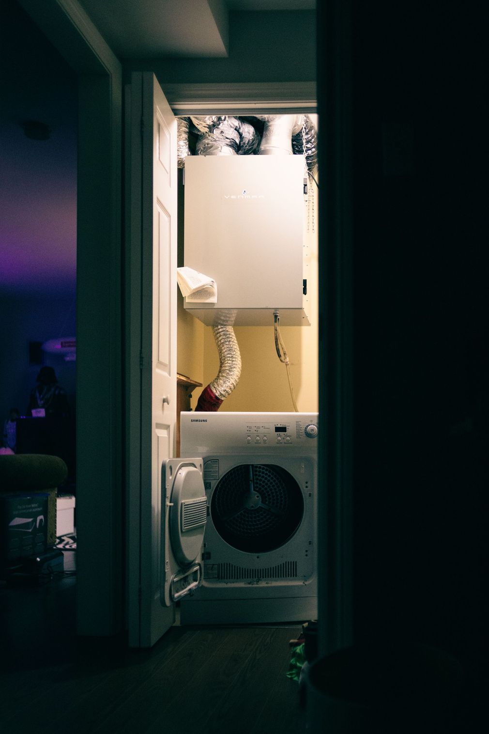 Dark hallway with stacked laundry machines and cabinets in a small utility closet