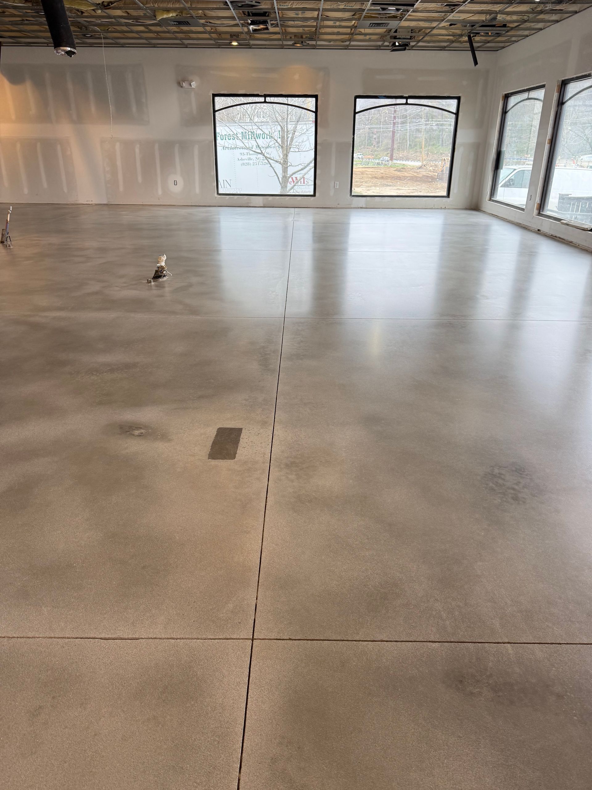 An interior view of a commercial space with a polished concrete floor and large windows under a partially finished ceiling.