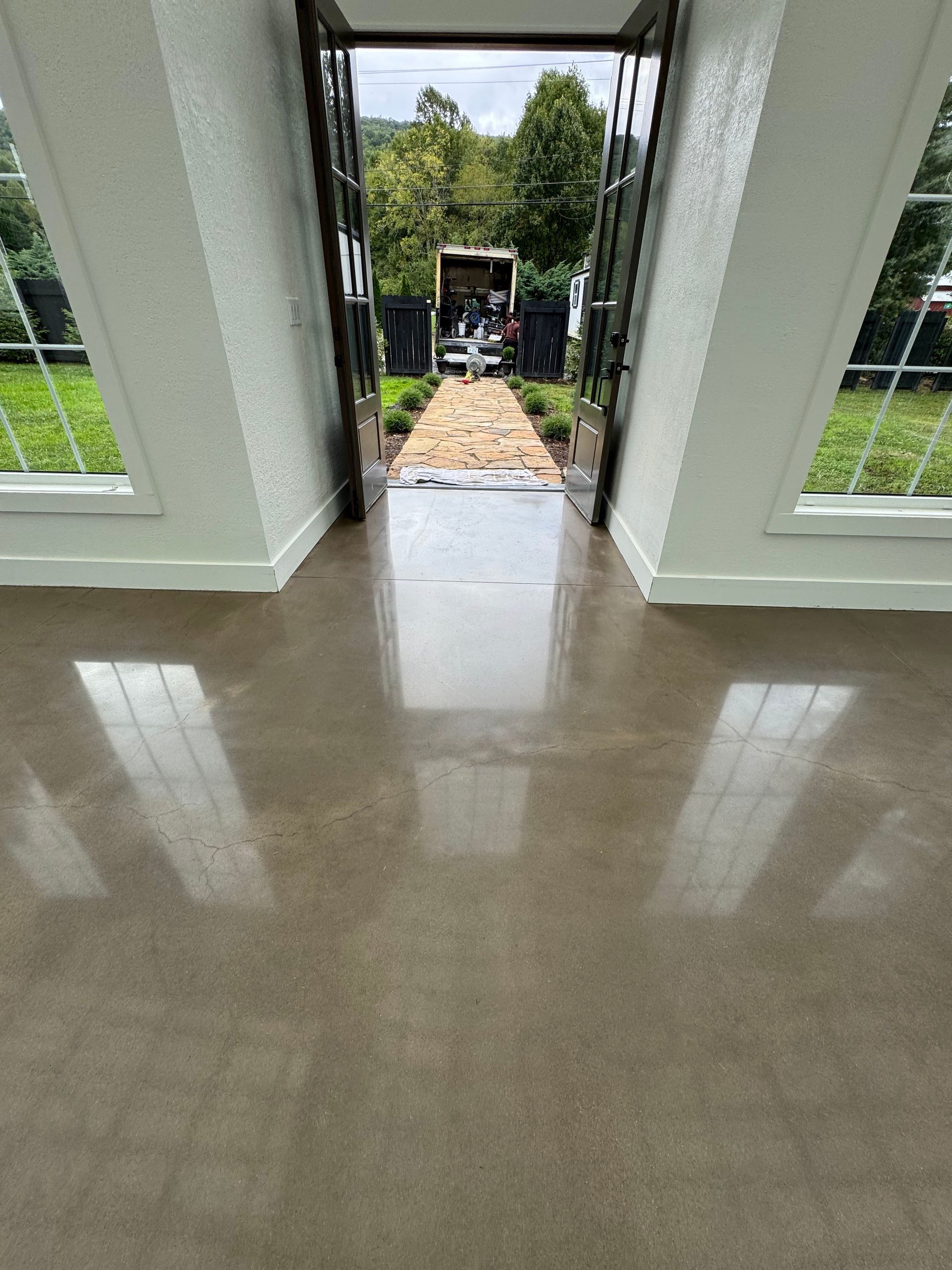 A polished concrete floor in a room with white walls and open doors leading to a stone path and a building outdoors.