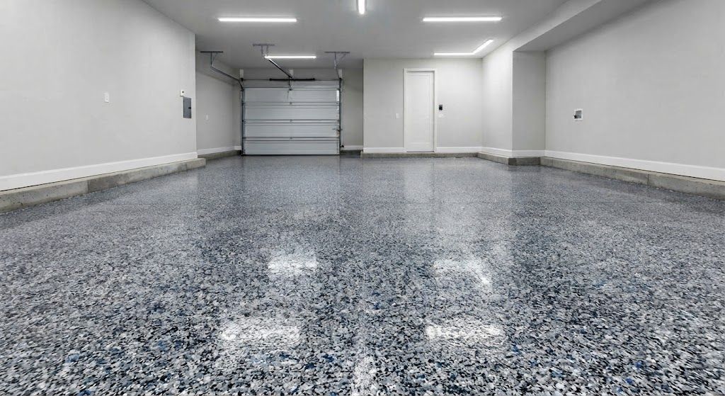 Empty indoor garage with gray speckled floor, white walls, and overhead lights