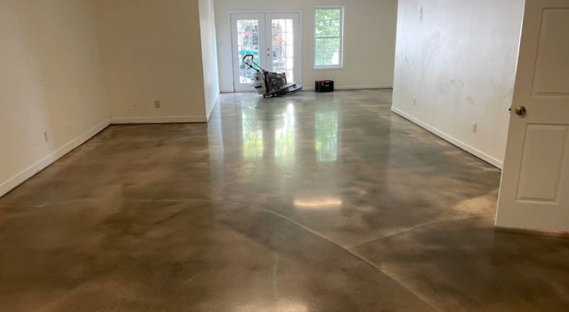 An empty room with polished, mottled brown concrete floors, white walls, and a glass door leading to the outdoors.
