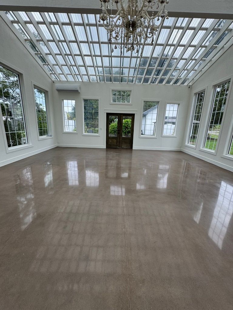 A bright, empty room with a high glass ceiling, beige polished floors, tall windows, and a central chandelier.