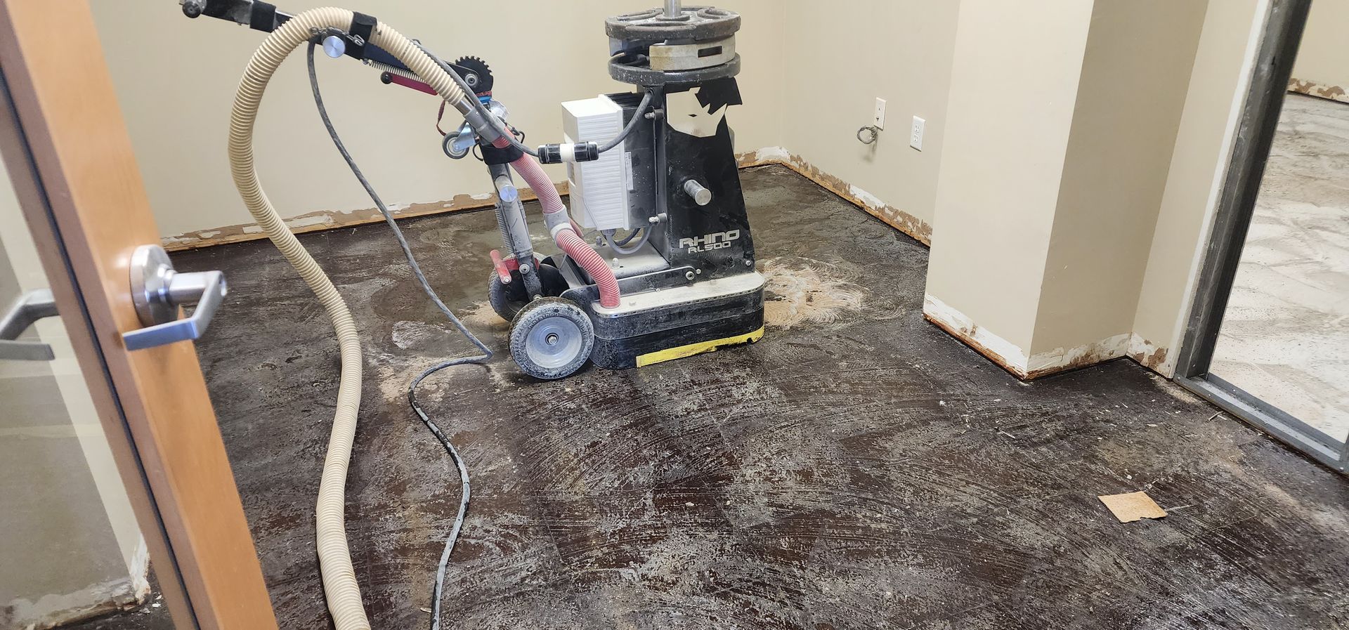 Floor grinder polishing a dark concrete floor in a room with beige walls and doorway.
