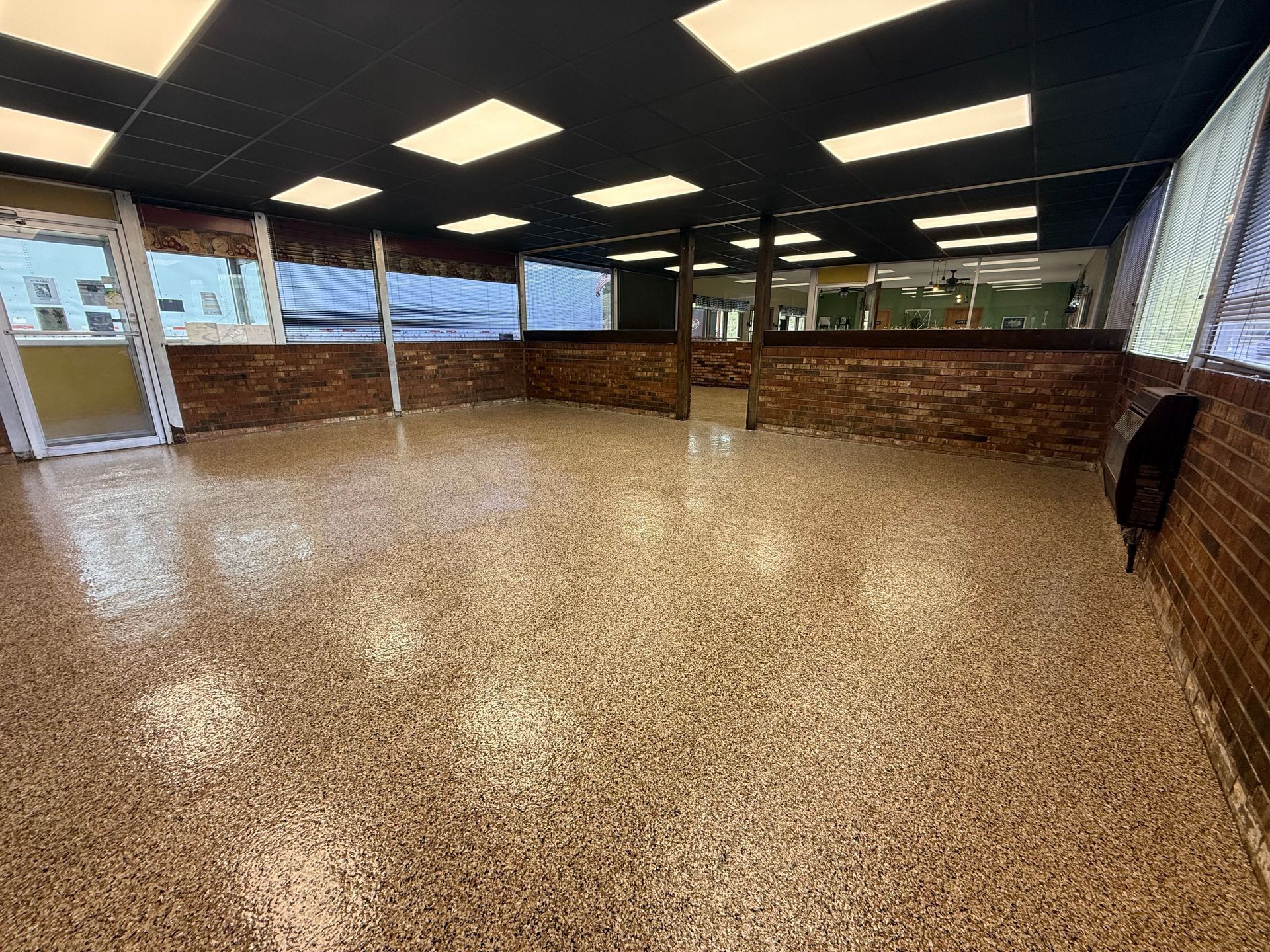 An empty commercial space with a speckled epoxy floor, brick lower walls, a dark ceiling with lights, and large windows.