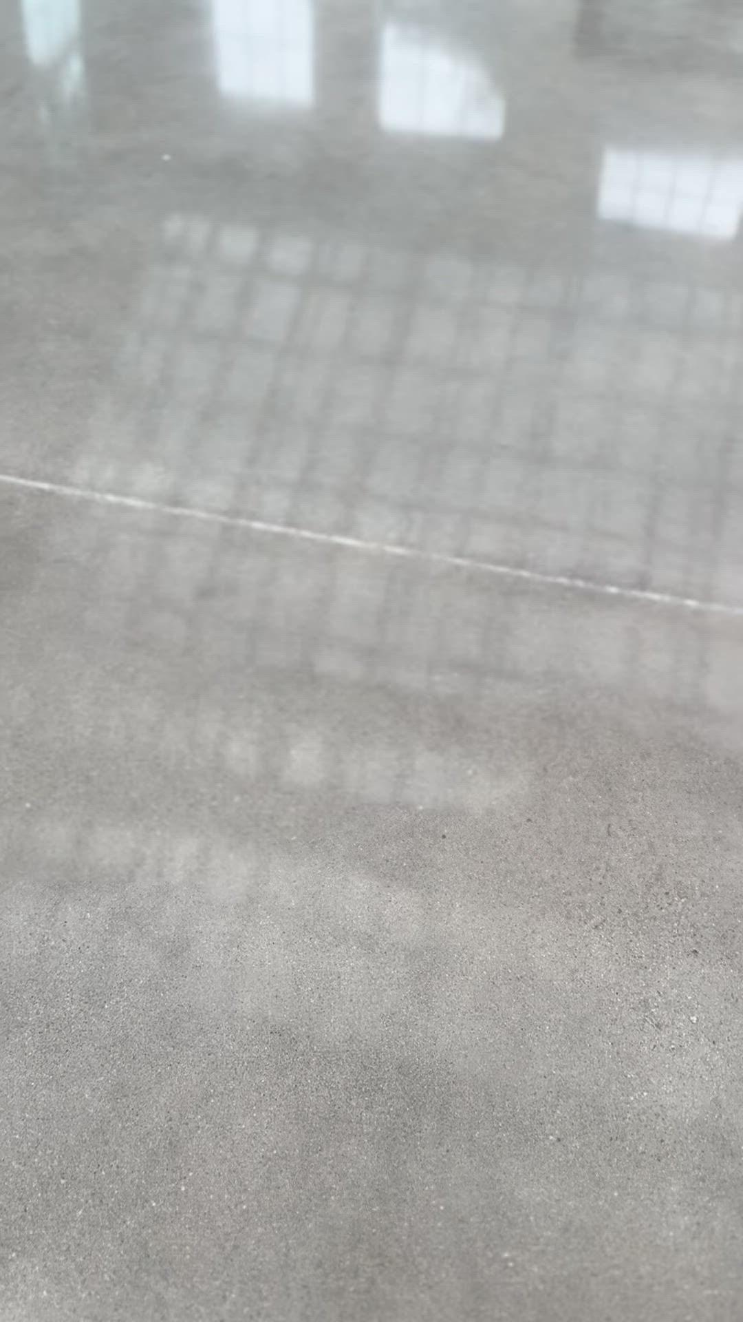 A polished, light-grey concrete floor with bright, grid-like light reflections from windows above.