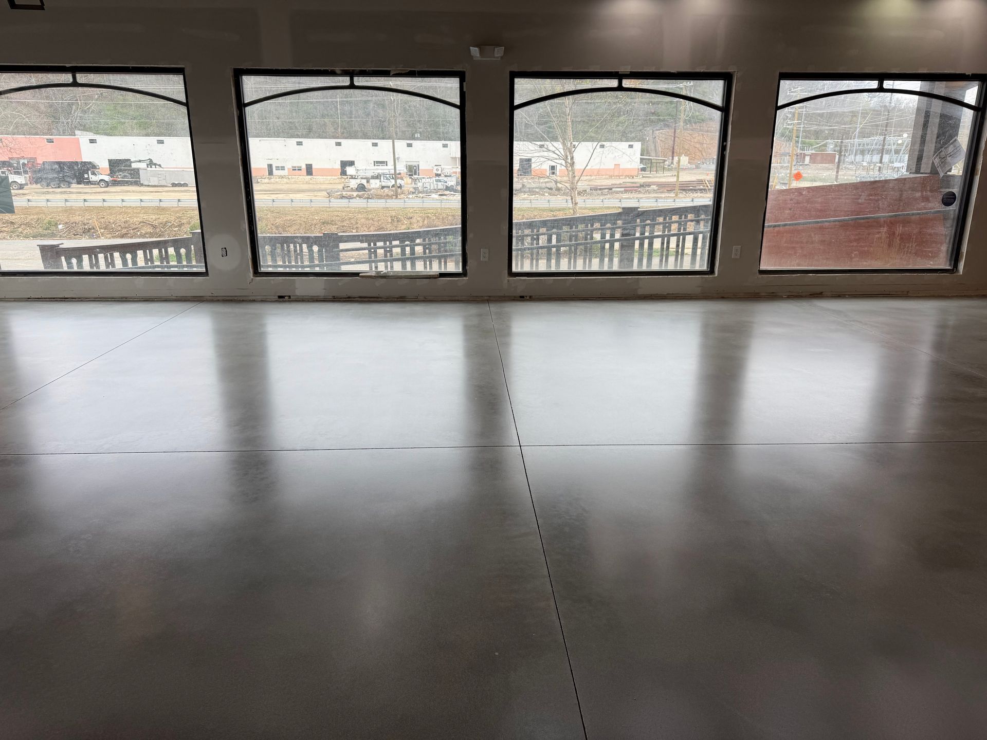 A polished concrete floor in a room with four large arched windows looking out onto a parking lot and building.