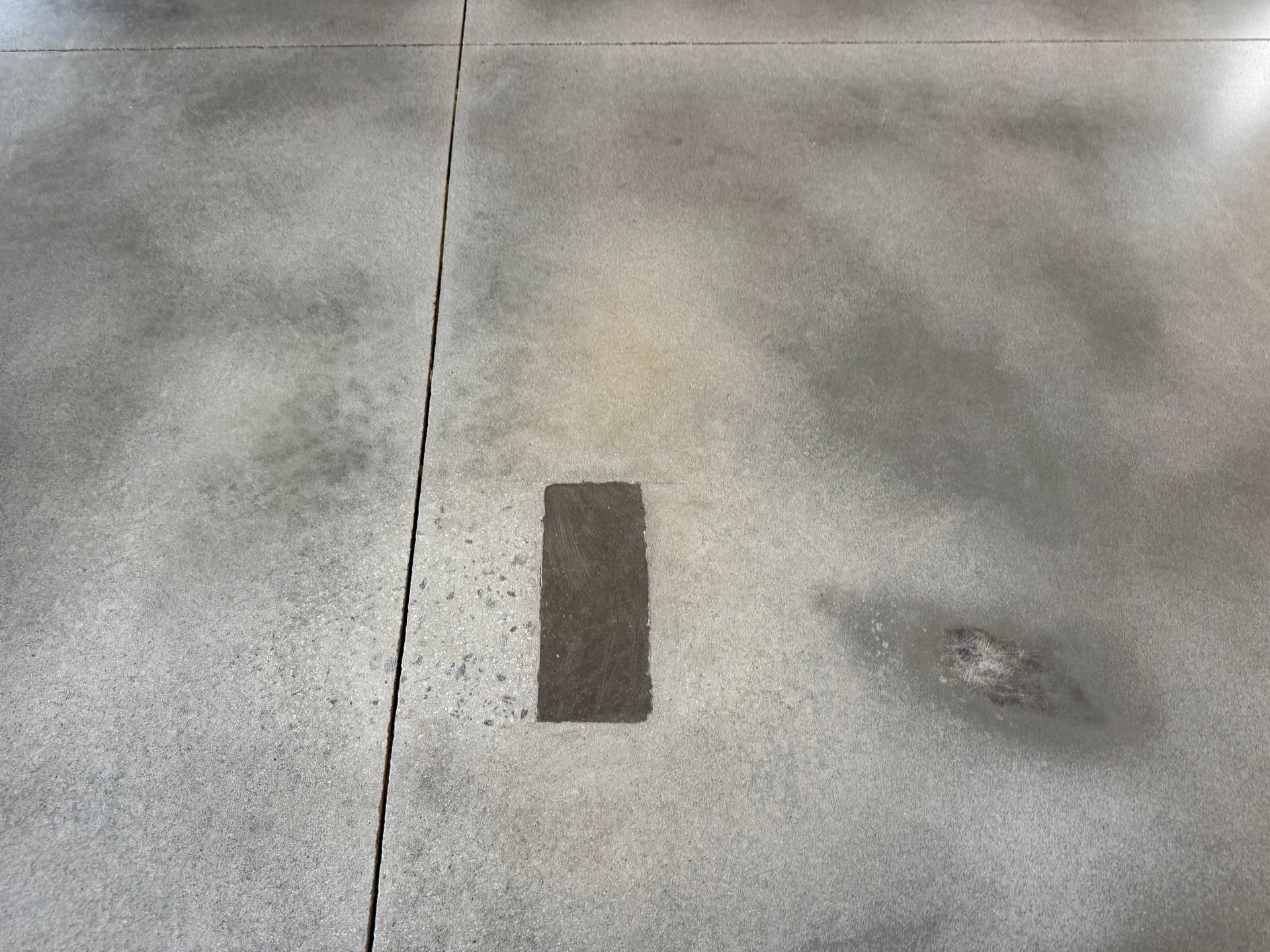 A concrete floor with a vertical expansion joint, a small rectangular patch, and a faded circular stain.