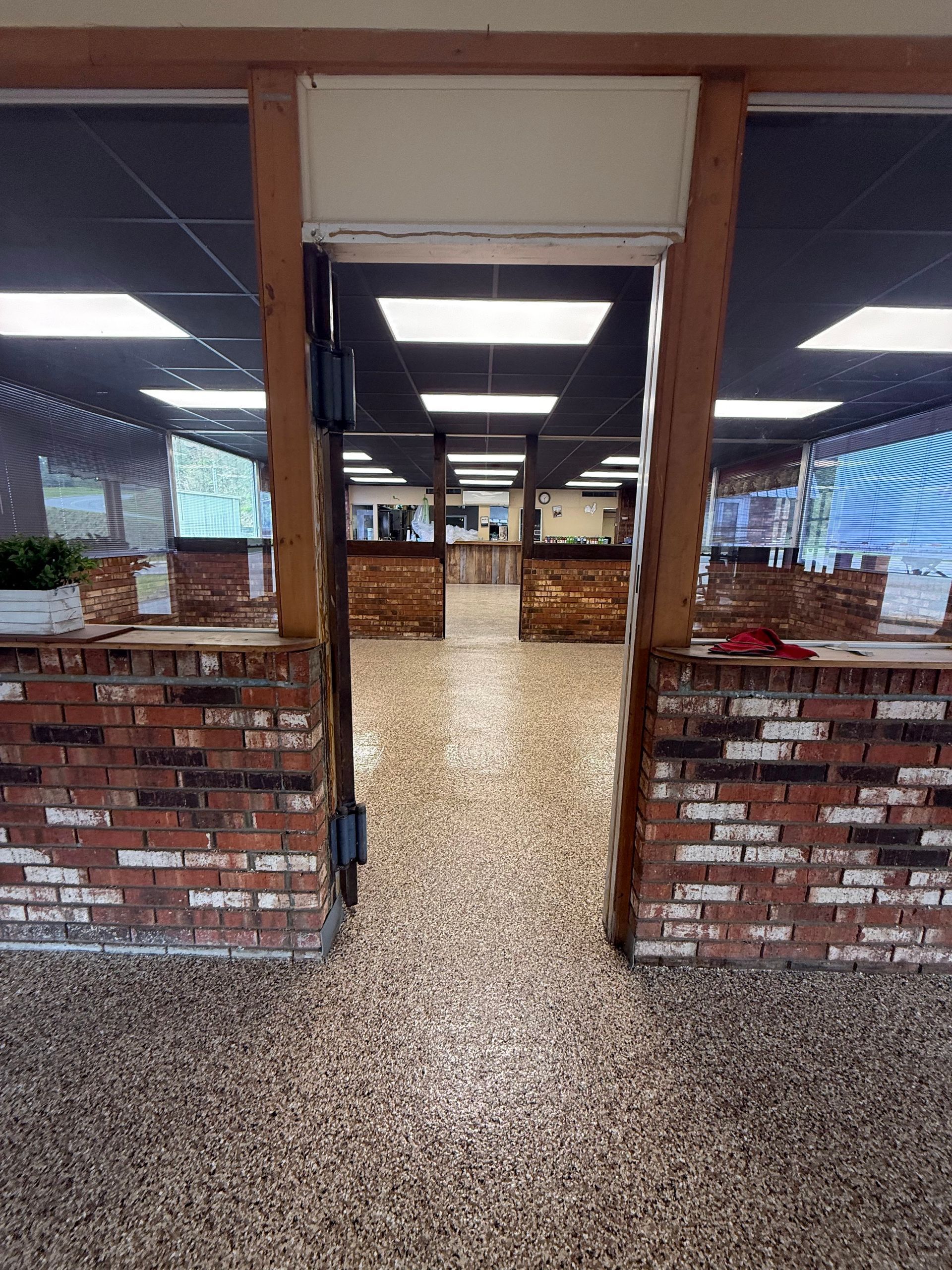 An indoor view looking through a wooden doorway frame into a room with brick counters and a speckled floor.