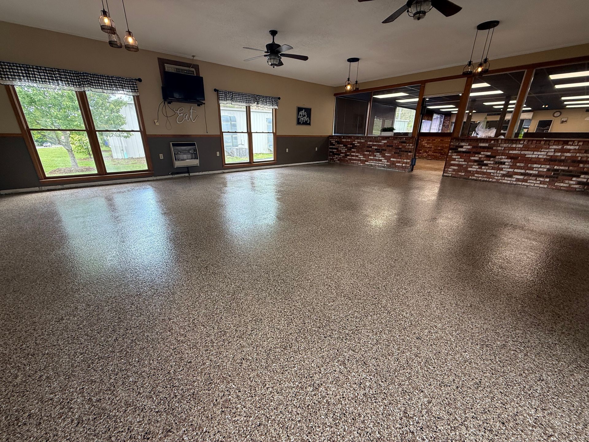 Spacious, modern basement with a speckled epoxy floor, ceiling fans, recessed lighting, and a rustic brick bar area.