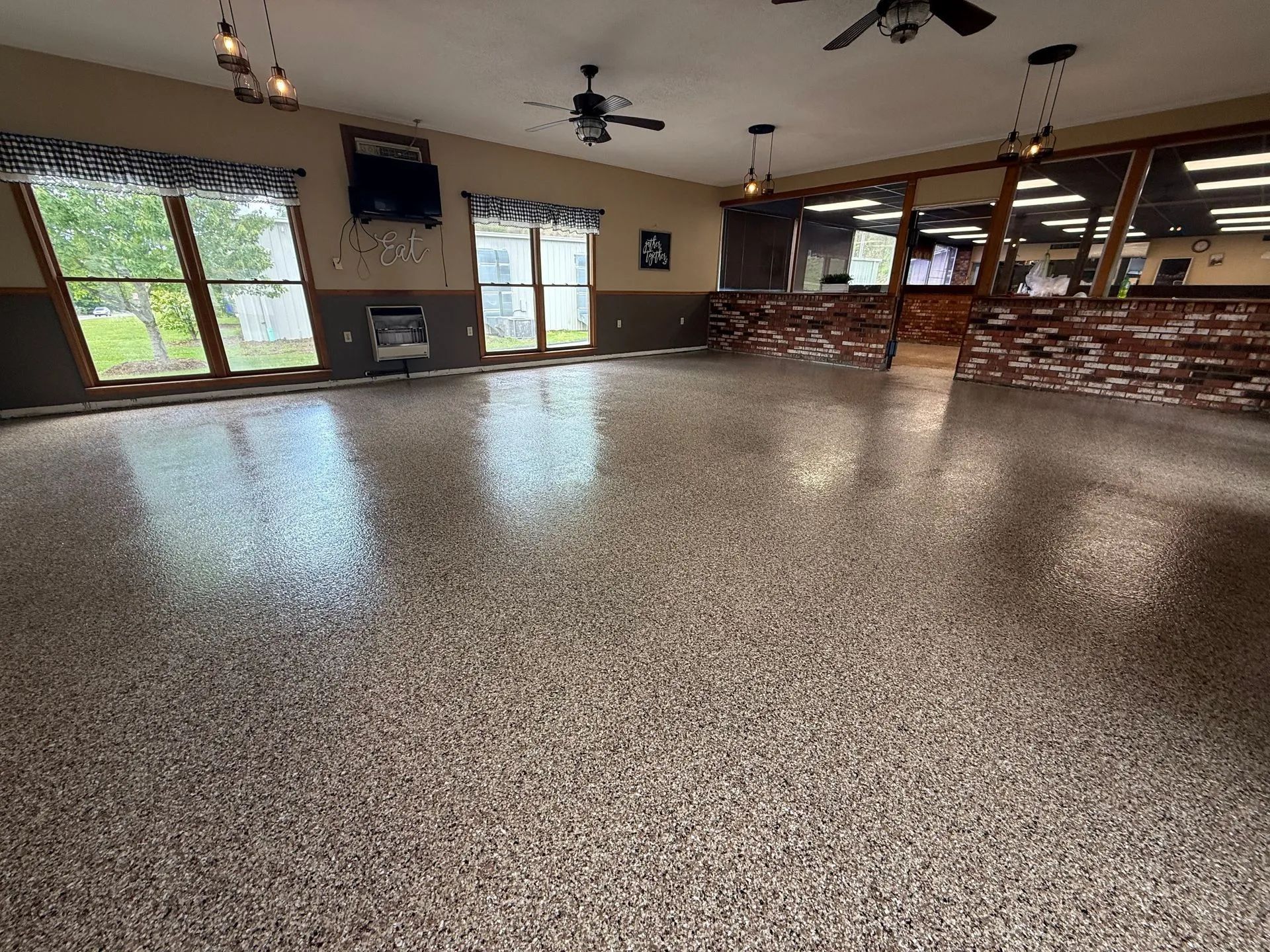 Empty community room with speckled floor, windows, ceiling fans, and a bar counter in the back.
