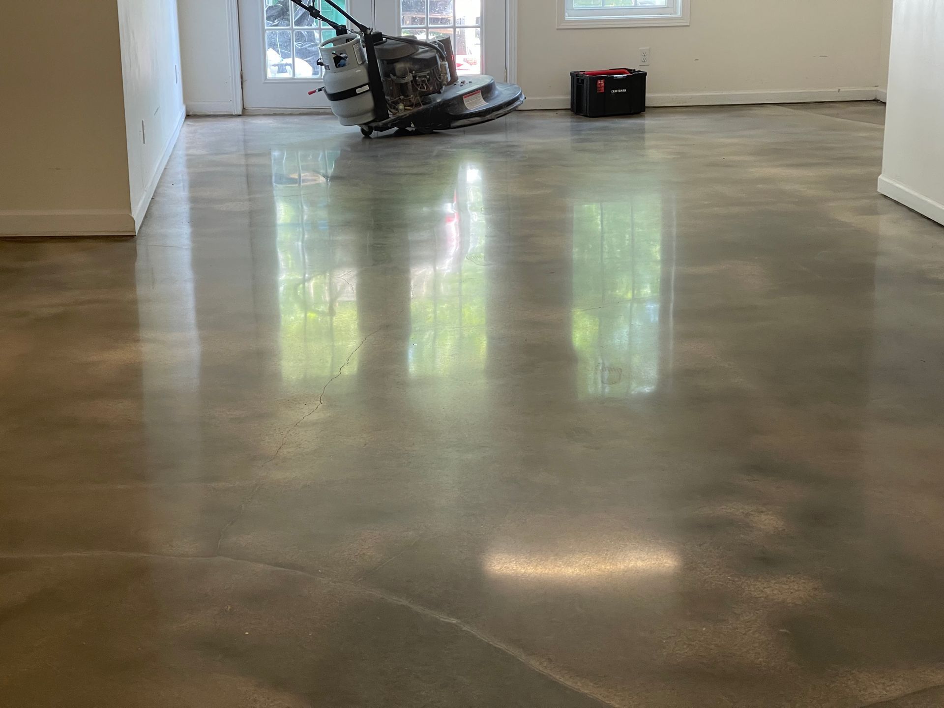 Polished, reflective concrete flooring in an interior room with a floor buffer machine in the background.