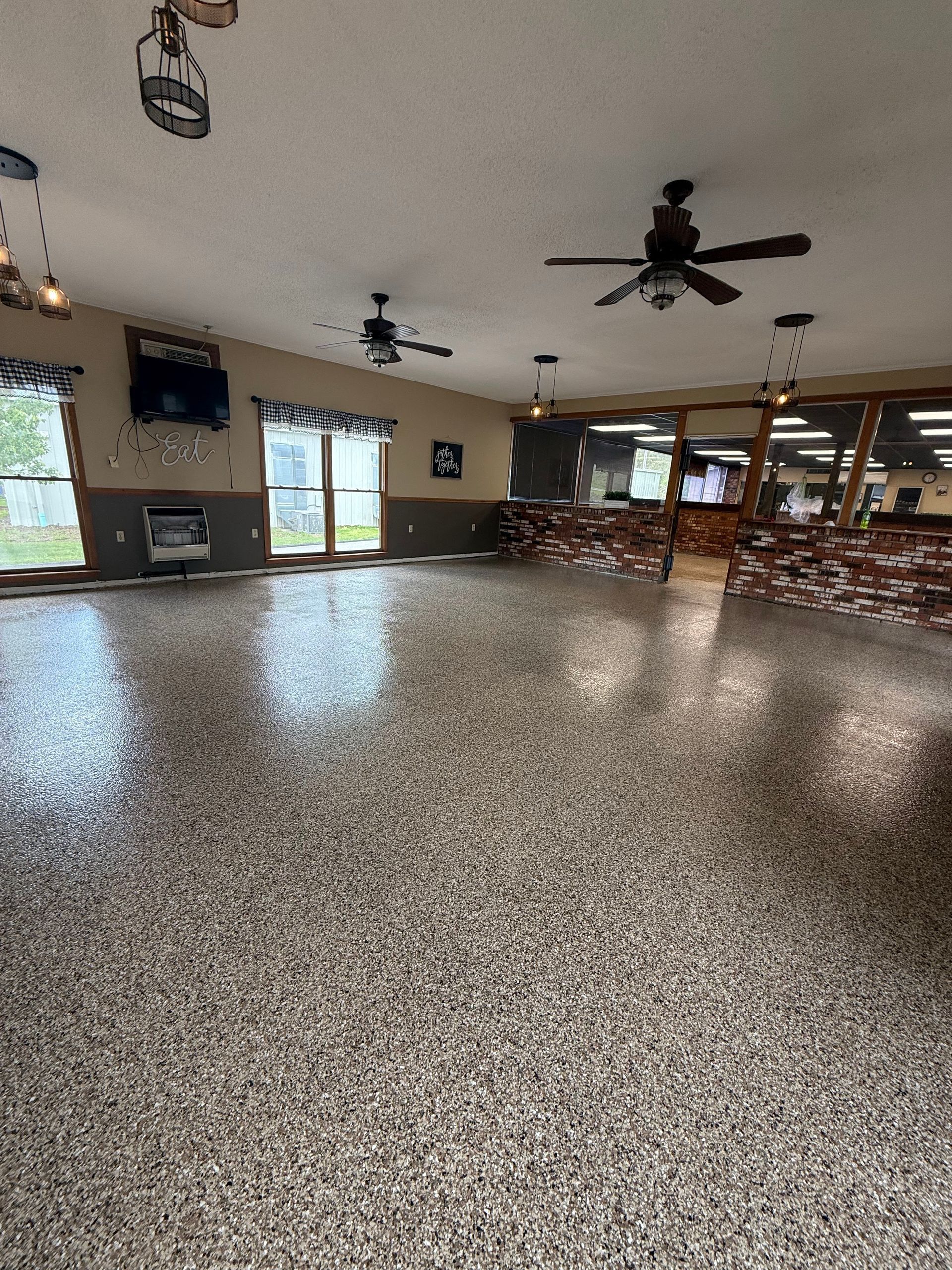 A large room with a high-gloss, speckled gray epoxy floor, ceiling fans, and a stone-accented counter area.