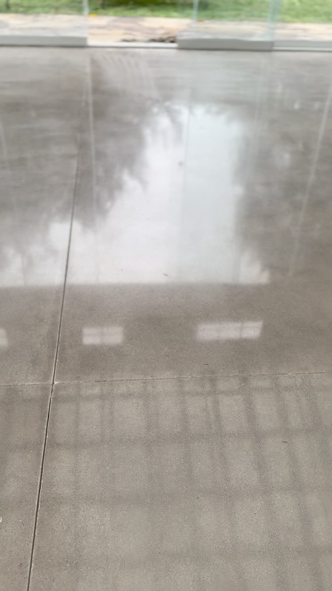 Polished gray concrete floor with a visible joint and reflections of windows and trees from outside.