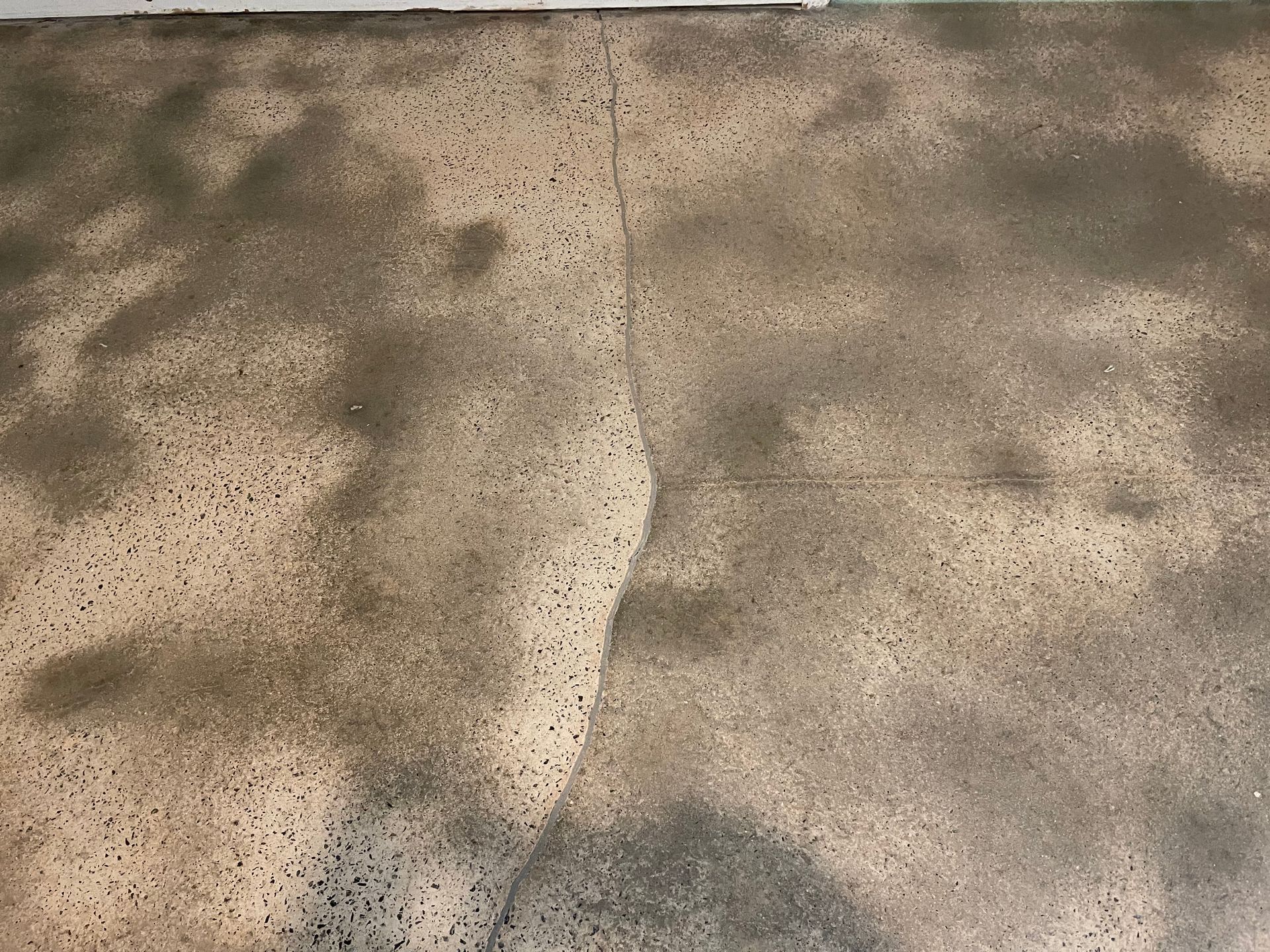 A vertical crack runs through mottled grey and beige concrete flooring with an exposed aggregate finish.