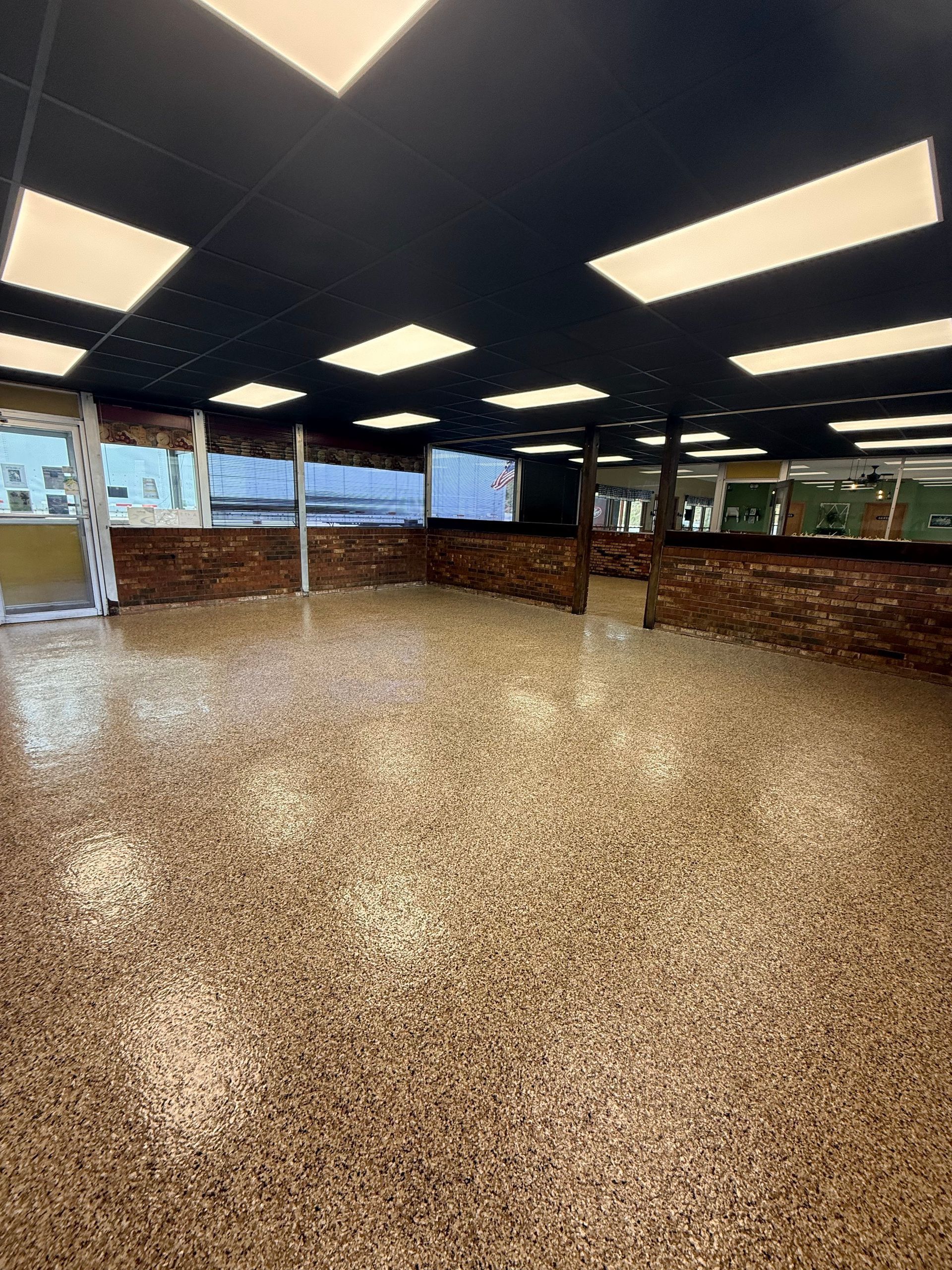 A bright, modern indoor space with a speckled epoxy floor, dark ceiling with recessed lighting, and brick-accented walls.