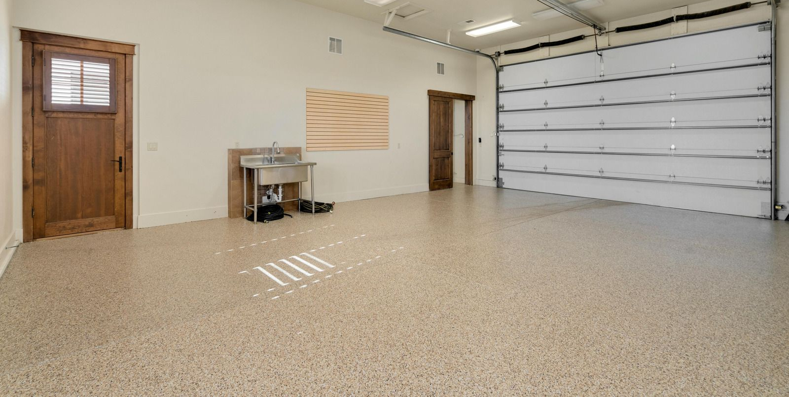 Empty garage with a speckled floor, white overhead door, and a wooden side door.