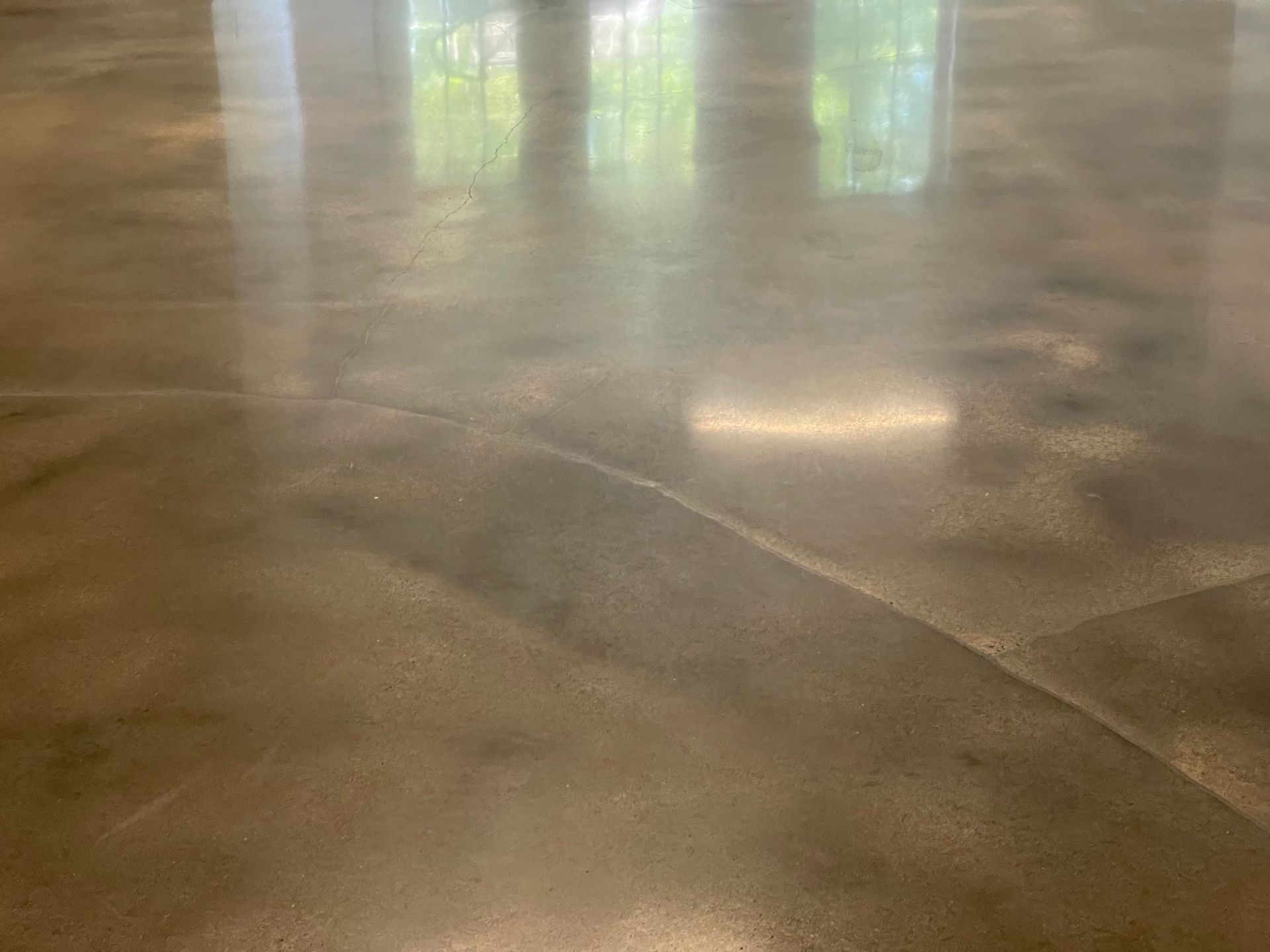 Polished concrete floor with a visible seam and reflections of windows and indoor lighting on the smooth surface.