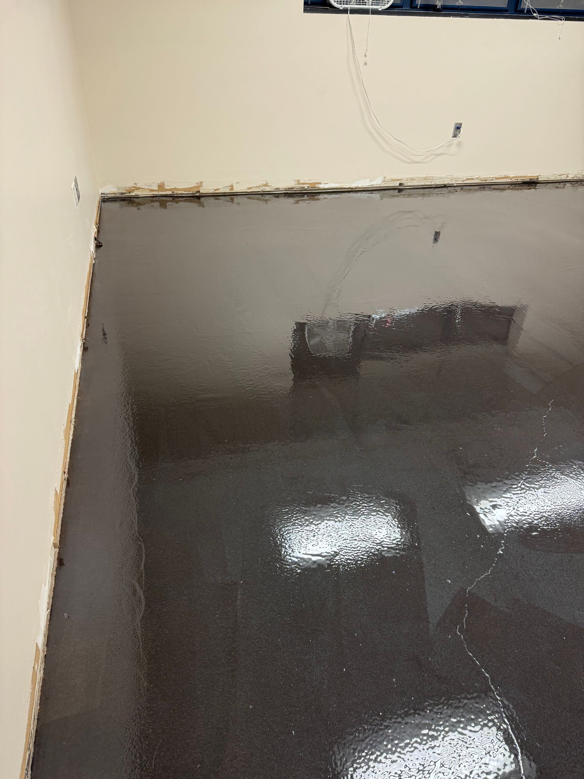 A newly poured, glossy dark gray epoxy floor in an unfinished room with light-colored walls and exposed wall edges.