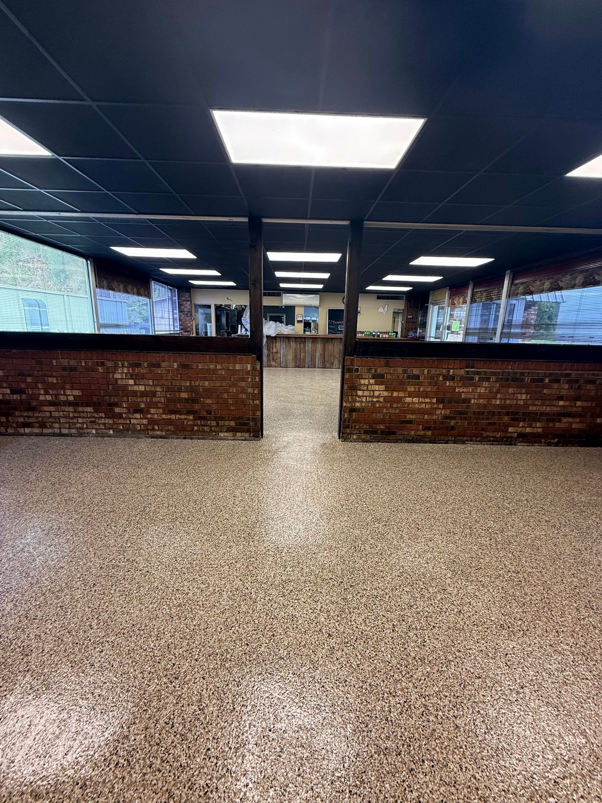 An indoor commercial space with a speckled floor, dark ceiling with recessed lights, and rustic, wood-paneled counters.