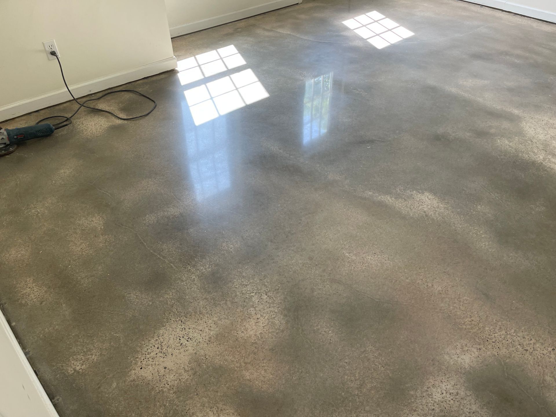 Polished concrete flooring reflects natural light from windows, with a power tool visible near the wall.