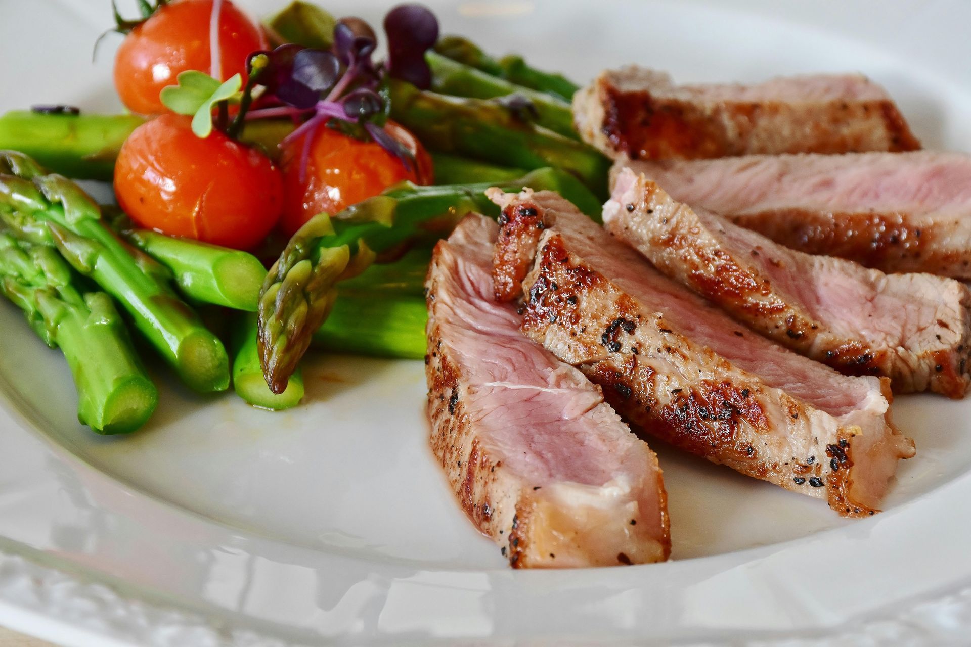 Une assiette blanche garnie de viande, d'asperges et de tomates.