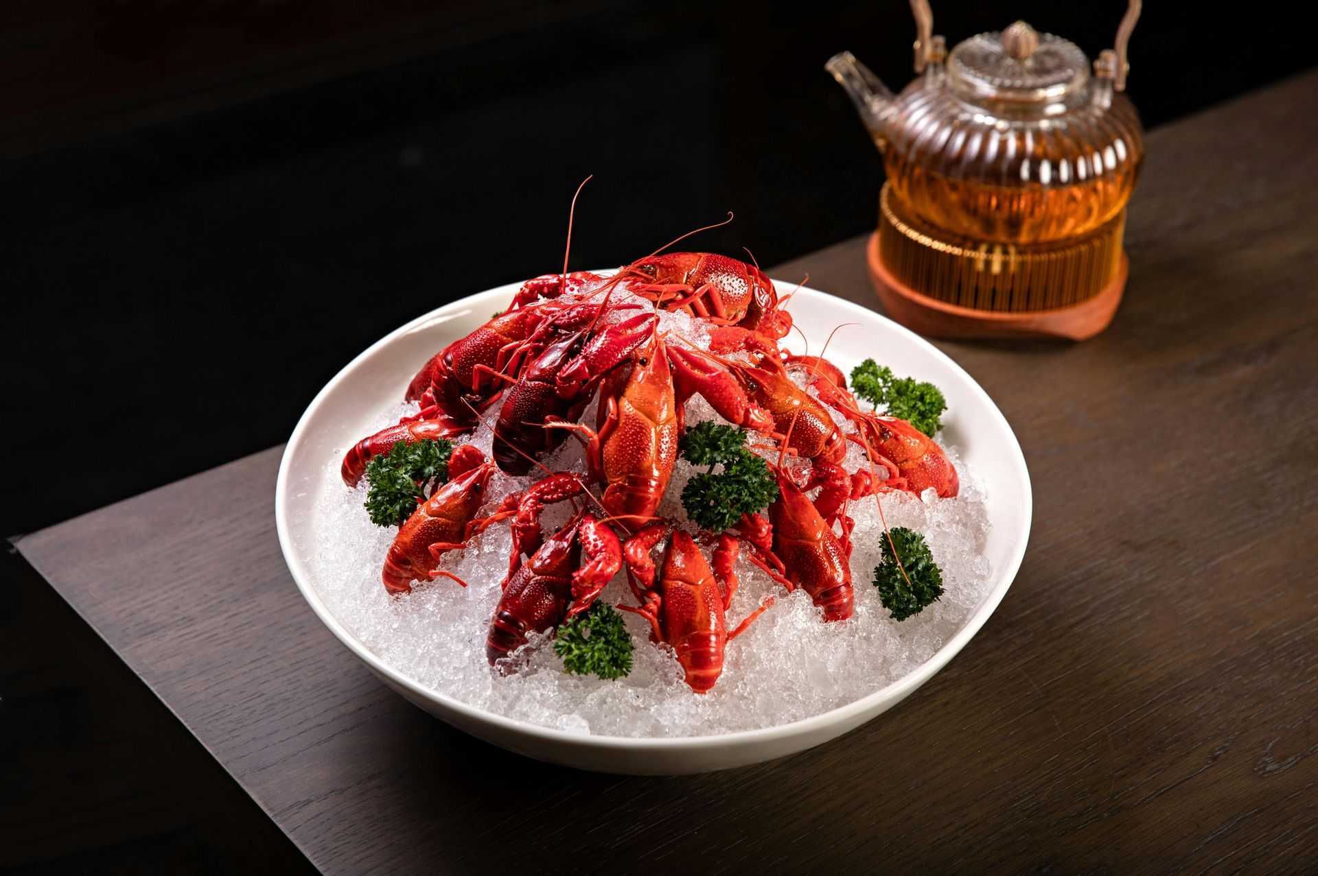 Une assiette de homards sur glace à côté d'une théière sur une table.