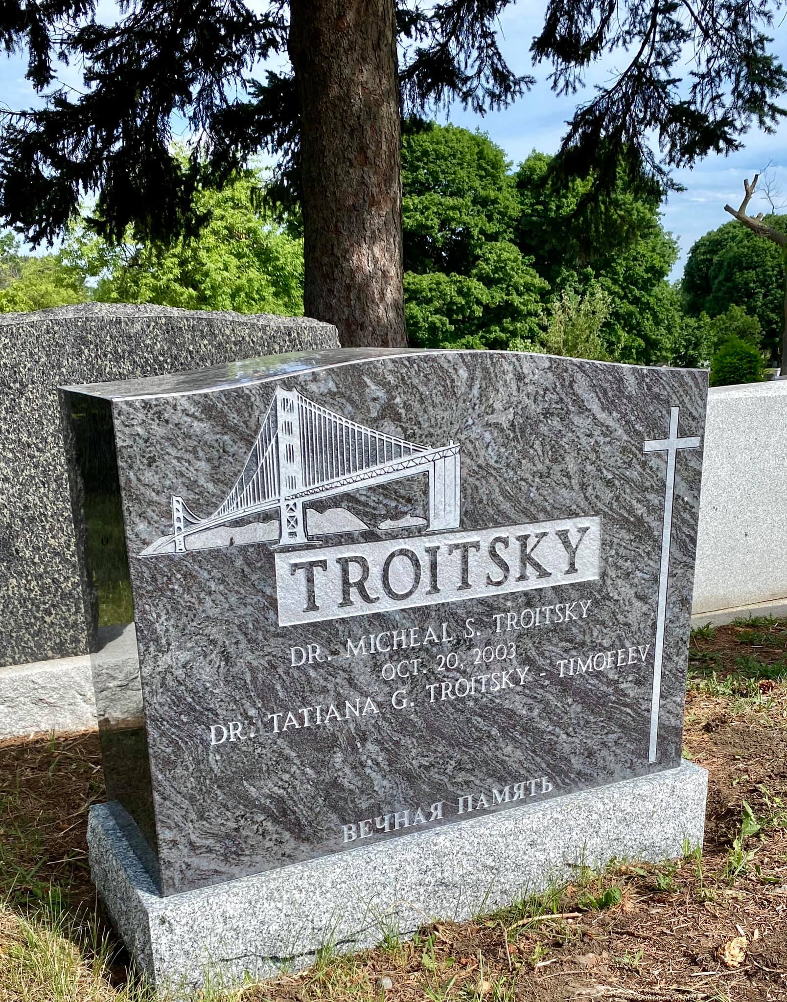 Pierre tombale grise ornée d'un motif de pont et portant l'inscription « Troitsky » dans un cimetière.